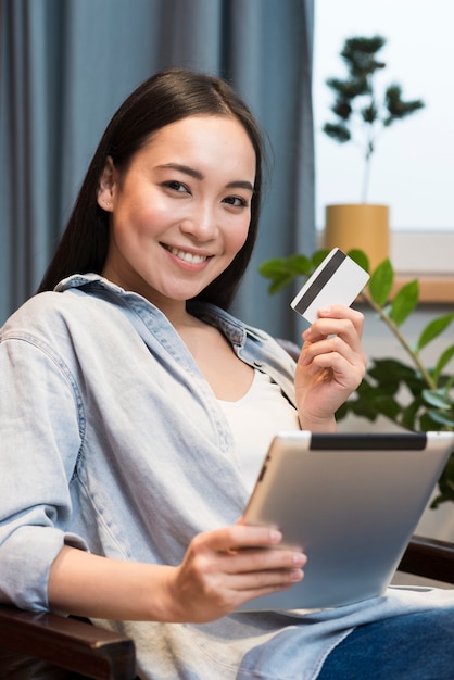 Mujer sonriente posando mientras sostiene la tableta y tarjeta de crédito
