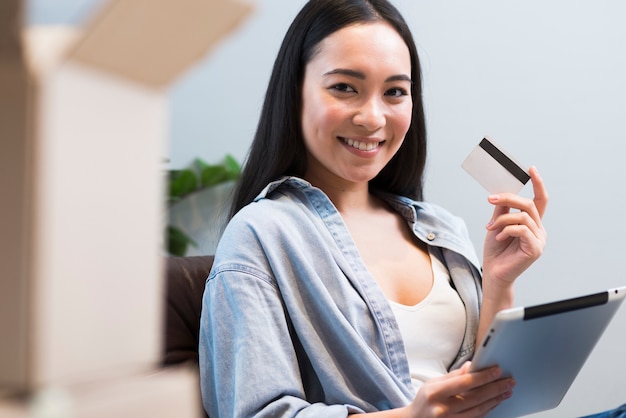 Mujer sonriente posando mientras sostiene la tarjeta de crédito y tableta