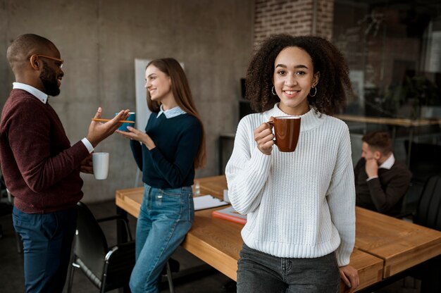 Mujer sonriente posando mientras sostiene la taza de café durante una reunión de oficina