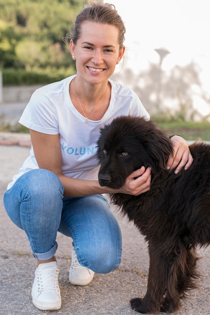 Mujer sonriente posando con perro negro esponjoso al aire libre