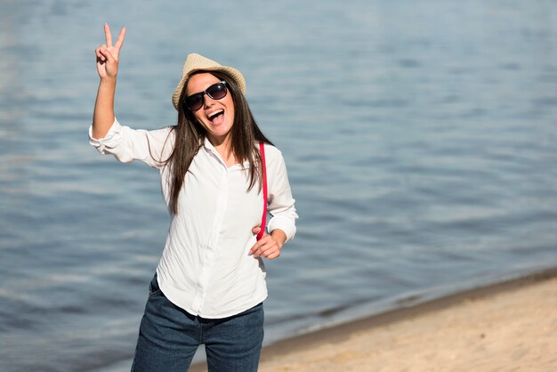 Mujer sonriente posando en la playa y haciendo el signo de la paz