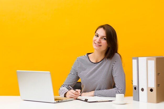 Mujer sonriente posando en su escritorio mientras escribe algo