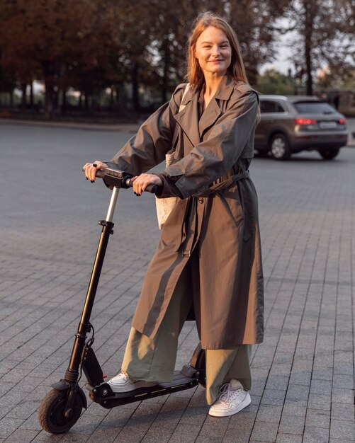 Mujer sonriente posando con su scooter eléctrico en la ciudad