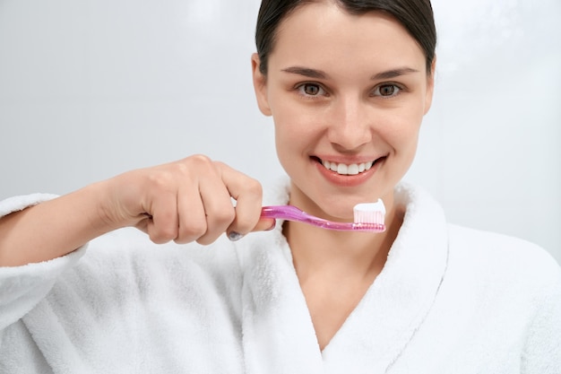 Mujer sonriente preparándose para limpiar los dientes en el baño.