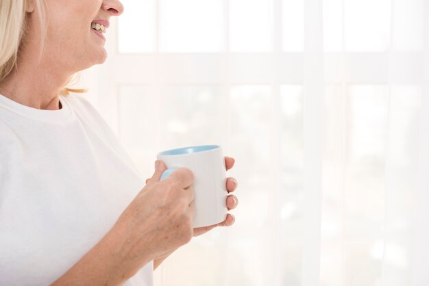 Mujer sonriente de primer plano con taza cerca de la ventana