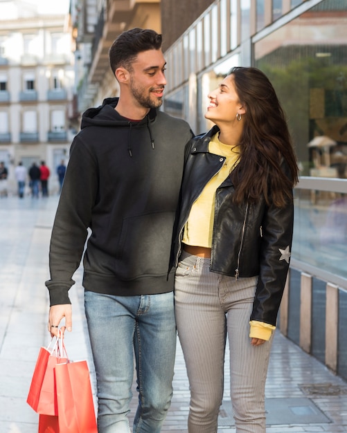 Mujer sonriente que abraza al hombre positivo joven con paquetes de las compras