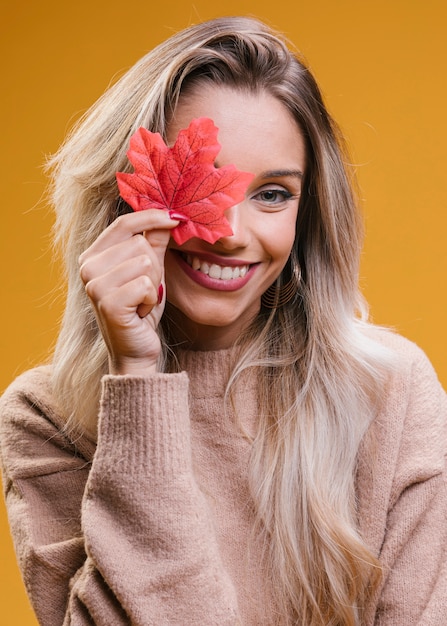 Mujer sonriente que cubre su ojo con la hoja de arce roja