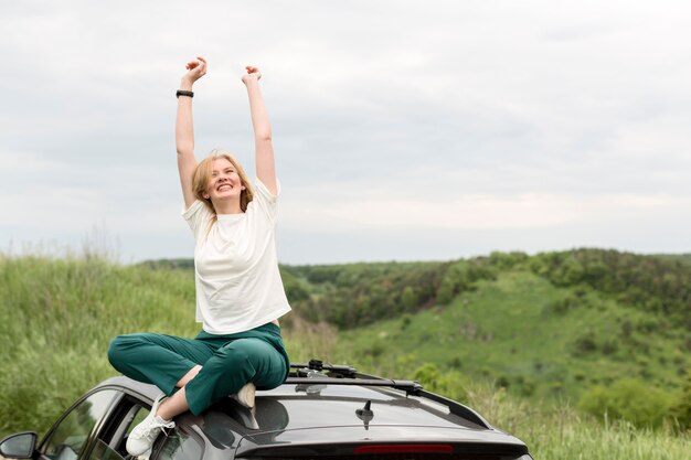 Mujer sonriente que disfruta de la naturaleza encima del coche