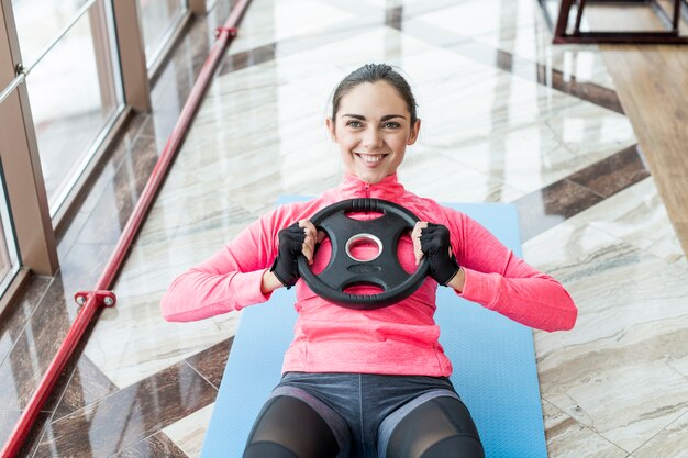 Mujer sonriente que ejercita los ABS con la placa del peso