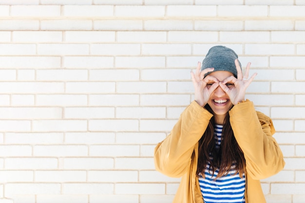 Foto gratuita la mujer sonriente que hace gesto aceptable tiene gusto de los prismáticos que desgastan la chaqueta y el sombrero hecho punto