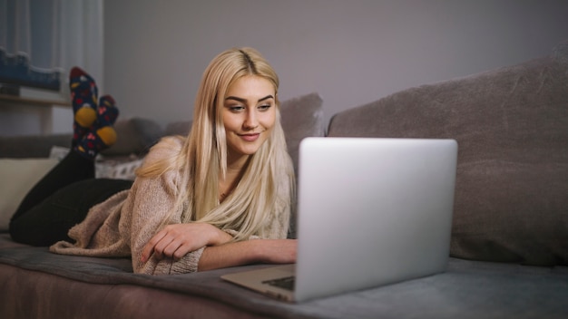 Mujer sonriente que hojea la computadora portátil en el sofá