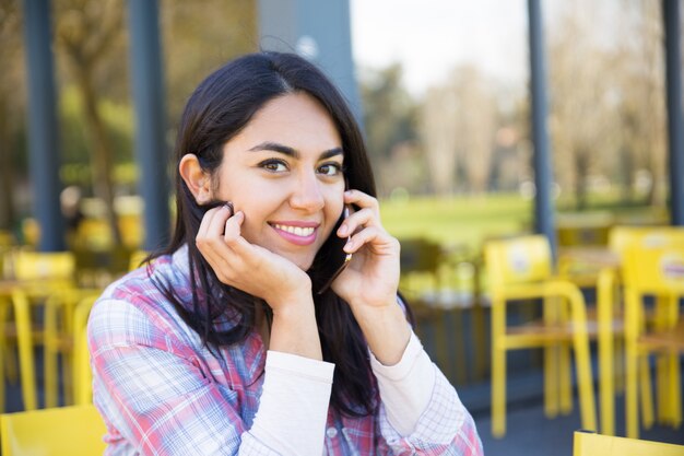 Mujer sonriente que invita al teléfono móvil en café al aire libre