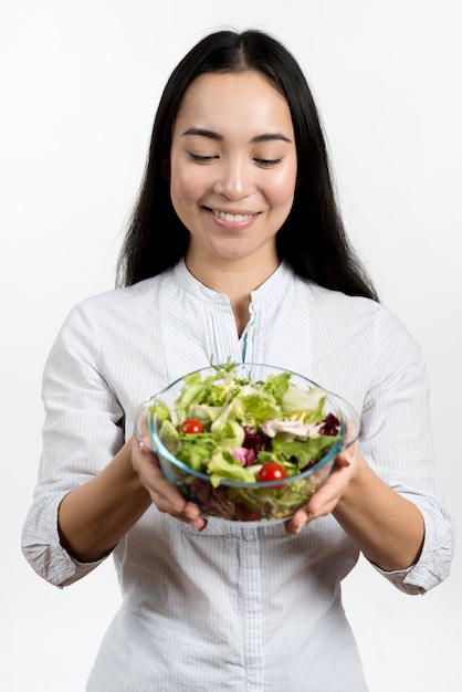 Mujer sonriente que mira el cuenco de ensalada sana contra el fondo blanco