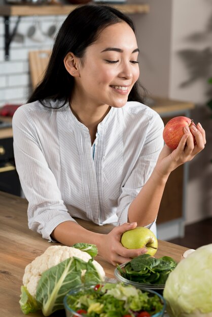 Mujer sonriente que mira la manzana roja en cocina en casa