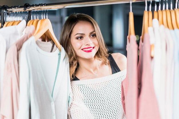 Mujer sonriente que mira la ropa que cuelga en el rastrillo en tienda