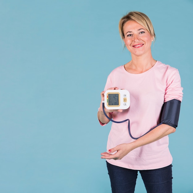 Mujer sonriente que muestra los resultados de la presión arterial en la pantalla del tonómetro eléctrico