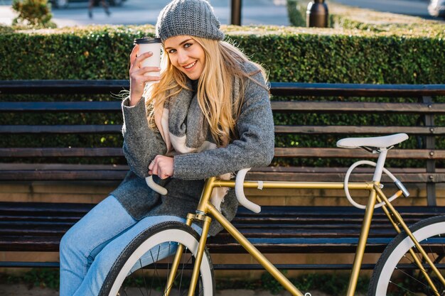 Mujer sonriente que muestra la taza cerca de la bicicleta