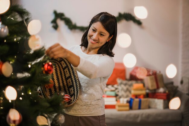 Mujer sonriente que pone los juguetes en el árbol