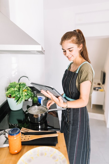 Mujer sonriente que prepara la comida que sostiene la tableta digital