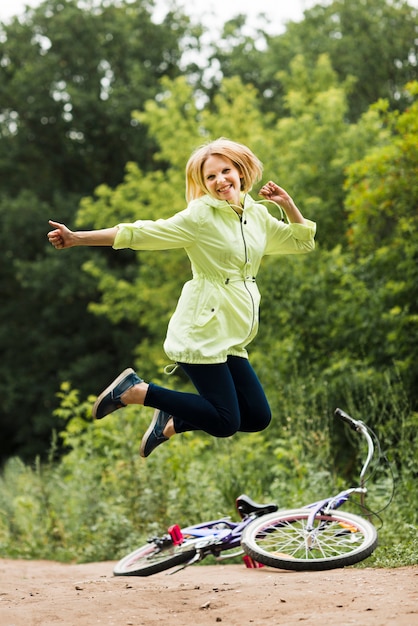 Foto gratuita mujer sonriente que salta con la bicicleta en fondo