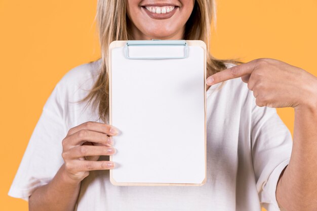 Mujer sonriente que señala el dedo en el libro blanco en blanco en el portapapeles