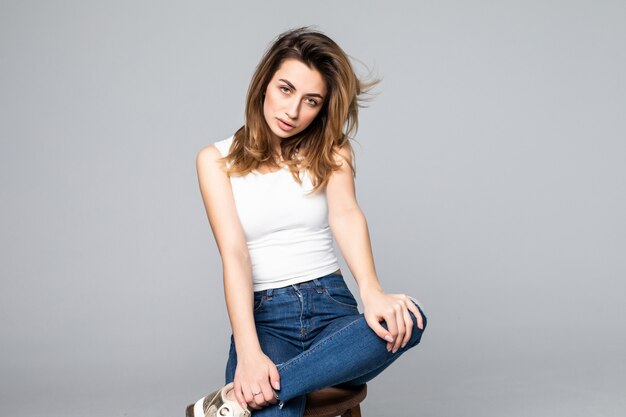 La mujer sonriente que se sentaba en taburete alto aisló el retrato del estudio con la pared gris.