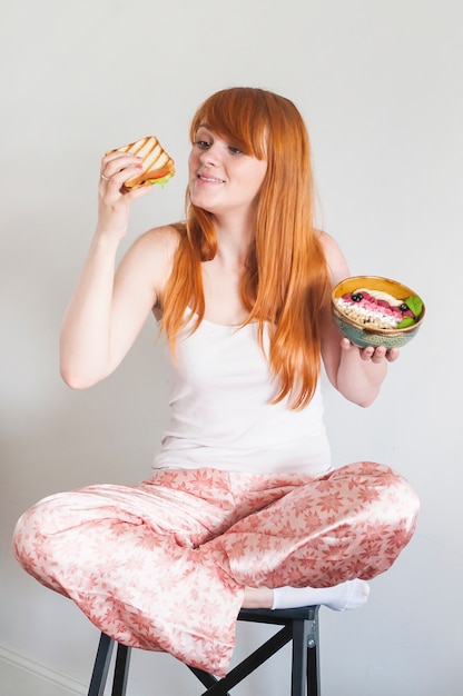 Mujer sonriente que se sienta en el taburete que sostiene el bocadillo y el cuenco de harina de avena