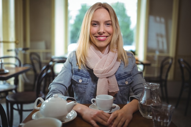 Mujer sonriente que se sienta con una taza de café en la cafetería ©