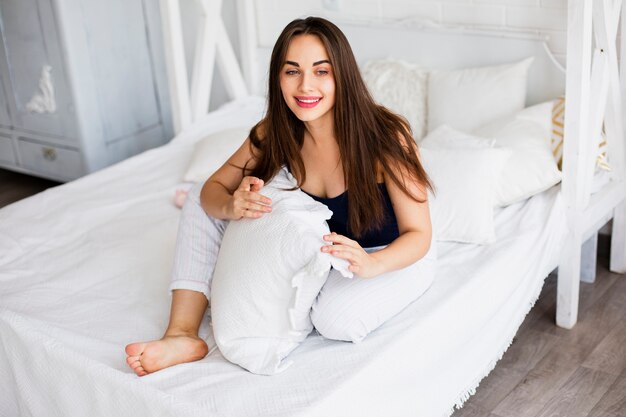 Mujer sonriente que sostiene la almohada en cama