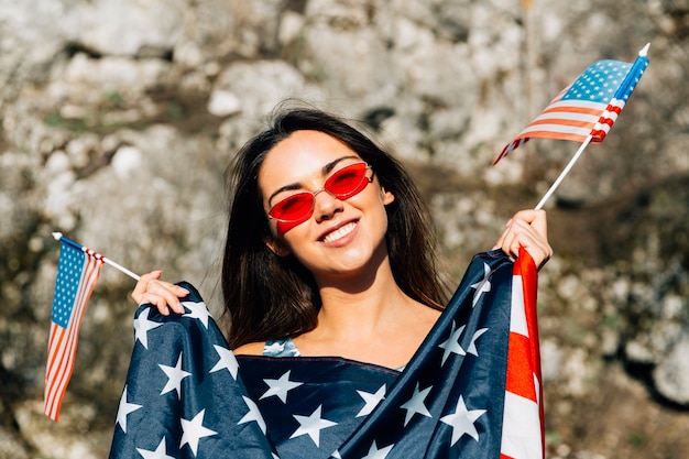 Foto gratuita mujer sonriente que sostiene banderas americanas en luz del sol