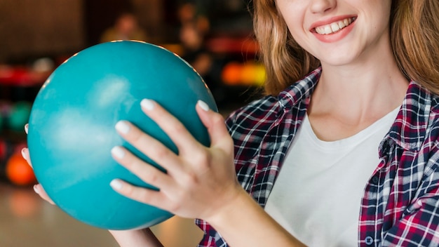Mujer sonriente que sostiene una bola de bolos turquesa