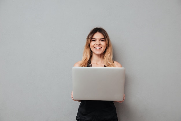 Foto gratuita mujer sonriente que sostiene la computadora portátil y que mira la cámara