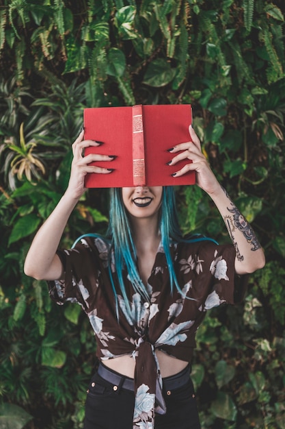 Mujer sonriente que sostiene el libro rojo delante de sus ojos