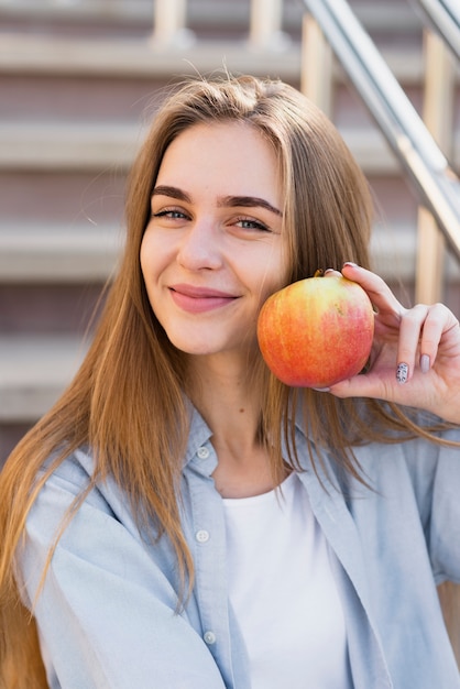 Foto gratuita mujer sonriente que sostiene una manzana cerca de su cara