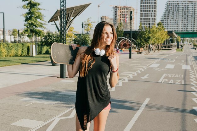 Mujer sonriente que sostiene el monopatín que se coloca en la calle