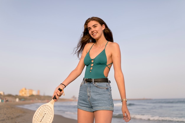 Mujer sonriente que sostiene la raqueta de tenis en la playa