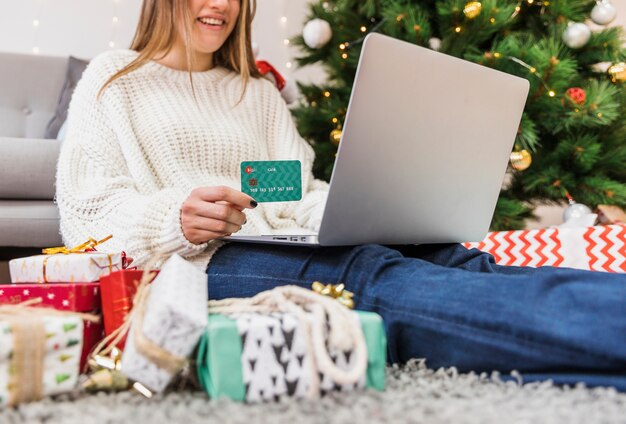 Mujer sonriente que sostiene la tarjeta de crédito y el ordenador portátil