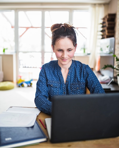 Mujer sonriente que trabaja en la computadora portátil en casa