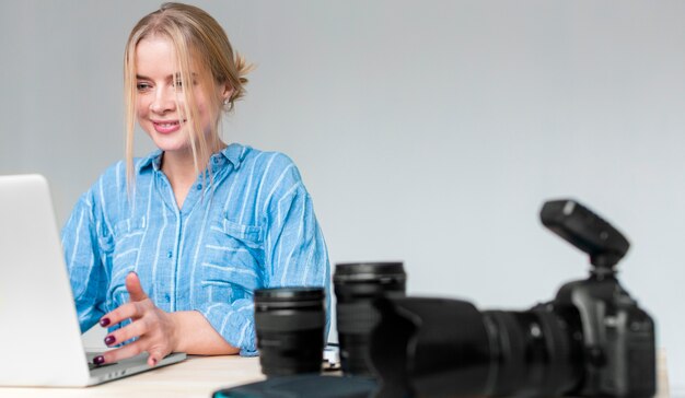 Mujer sonriente que trabaja en su computadora portátil y cámara con lente