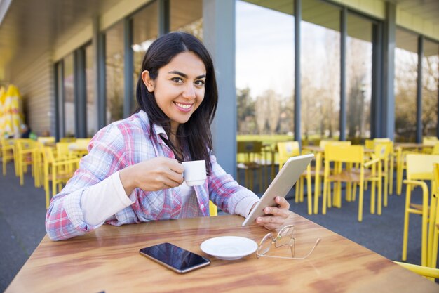 Mujer sonriente que usa los artilugios y tomando café en café