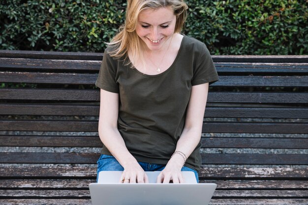 Mujer sonriente que usa la computadora portátil en banco