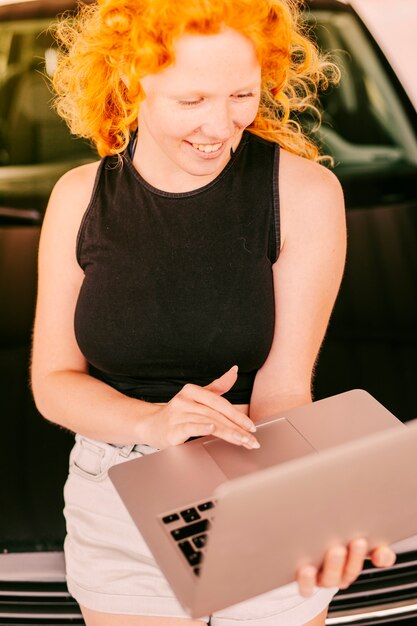 Mujer sonriente que usa la computadora portátil que se inclina contra el coche