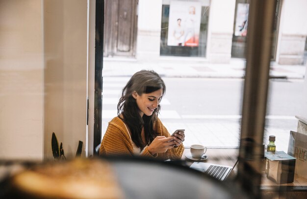 Mujer sonriente que usa smartphone en café