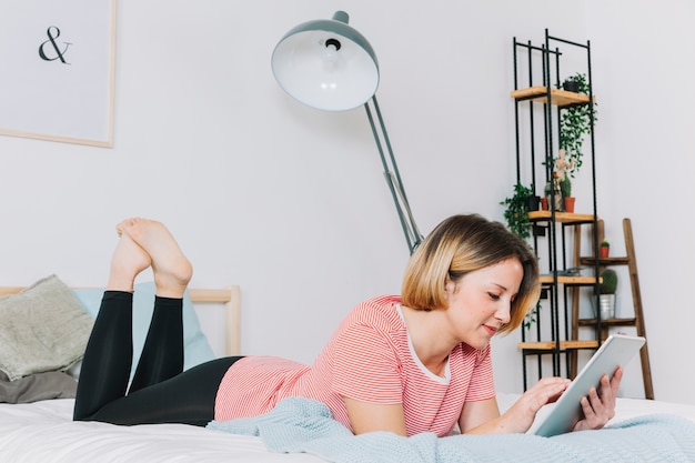 Mujer sonriente que usa la tableta en cama