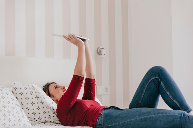 Mujer sonriente que usa la tableta en cama