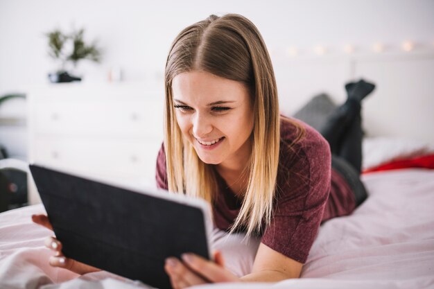 Mujer sonriente que usa la tableta en cama