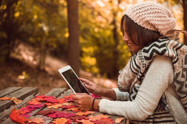 Mujer sonriente que usa la tableta en la mesa en el parque del otoño