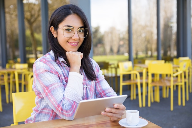 Mujer sonriente que usa la tableta y tomando café en café