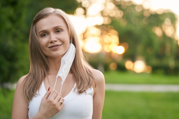 Mujer sonriente quitándose la mascarilla blanca