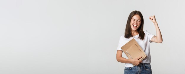 Mujer sonriente regocijándose sosteniendo cuadernos y bomba de puño alegre celebrando